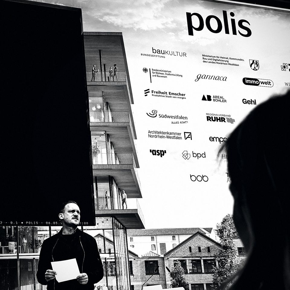 Christopher Peterka vor der polis-Partnerwand; das gannaca-Logo zwischen Bundesbauministerium, NRW-Heimatministerium und Bundesstiftung Baukultur.